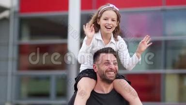 一个女学生的幸福女儿坐在她年轻父亲的肩膀上。 女孩高兴地挥动着双手